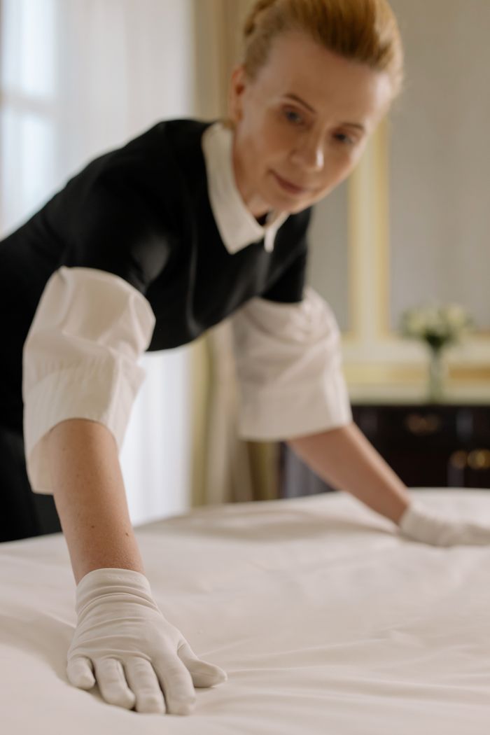 who-we-are A housekeeper elegantly arranges bed sheets in a luxurious hotel room, showcasing hospitality expertise.