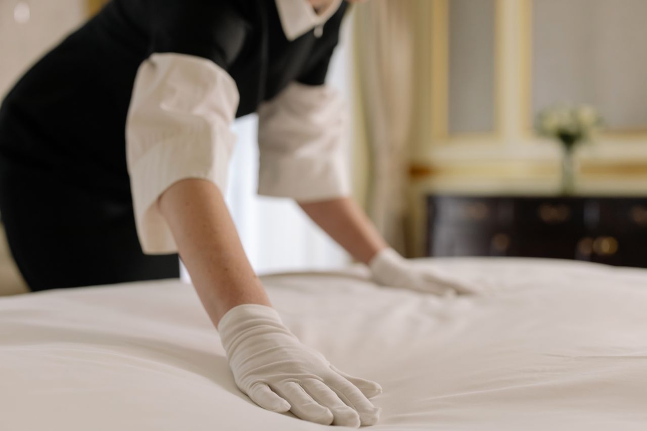 services-02 A housekeeper straightening the bed linens in a well-appointed hotel room.